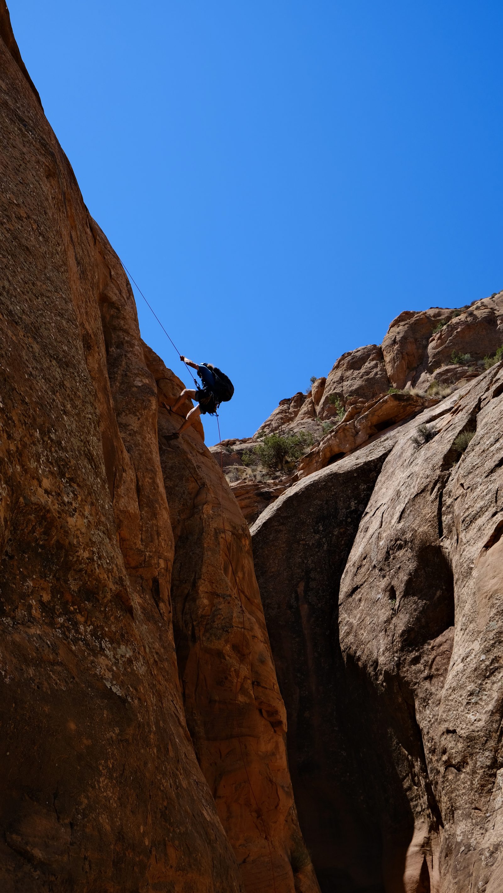 A first-time canyoneer rappelling down a red-rock wall with a NAVTEC guide belaying