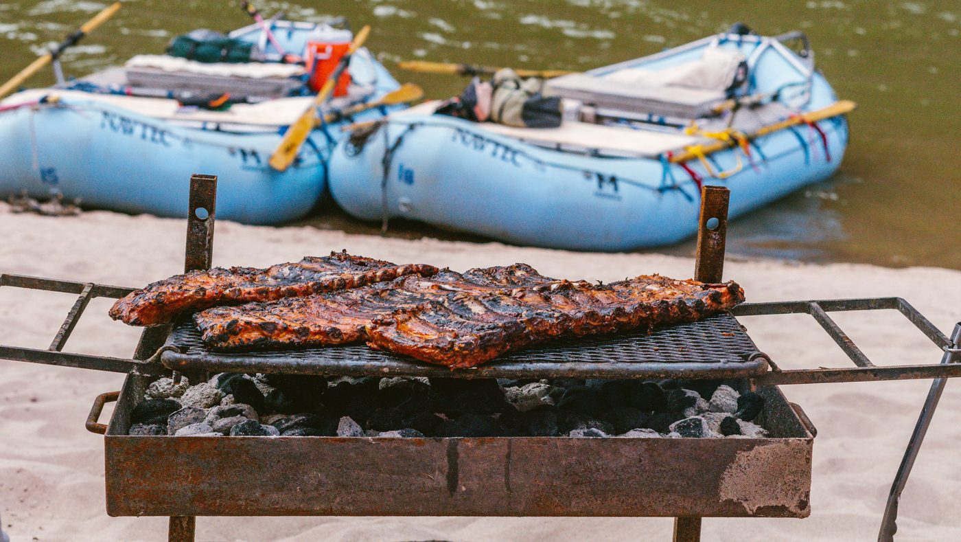 Ribs on the grill at a NAVTEC river camp with rafts beached behind